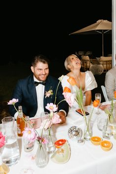 a man and woman sitting at a table with flowers in vases next to each other