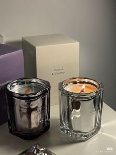 two candles sitting next to each other on top of a white table in front of boxes