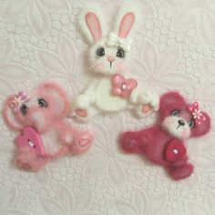 three small stuffed animals are sitting on a white surface with pink bows and hearts in their hands