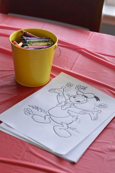 a bucket full of crayons sitting on top of a table next to a drawing