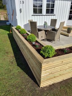 a wooden planter box sitting on top of a grass covered field next to a white building