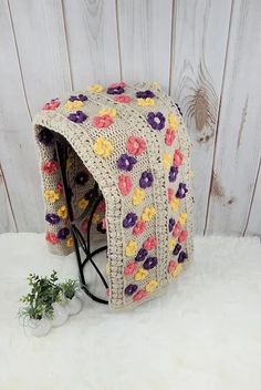 a crocheted hat with flowers on it sitting next to a white wooden wall