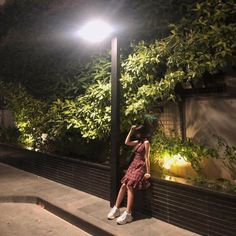 a woman leaning against a lamp post at night