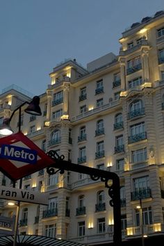 the metro sign is lit up in front of a large white building with windows and balconies