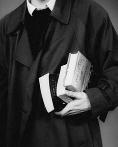 black and white photograph of a man holding two books in his hands while wearing a trench coat