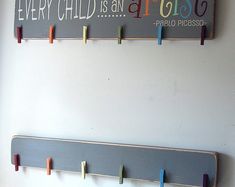 two wooden pegs are hanging on the wall next to a sign that says every child is an artist