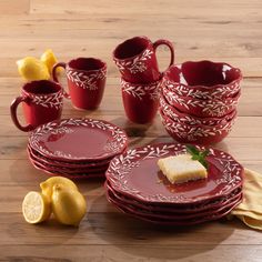 a table topped with red plates and cups filled with cake next to lemon wedges