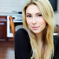 a woman with long blonde hair sitting in front of a stove top oven and looking at the camera