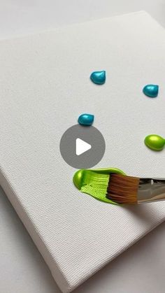 a paintbrush with green and blue drops on it sitting next to a white canvas