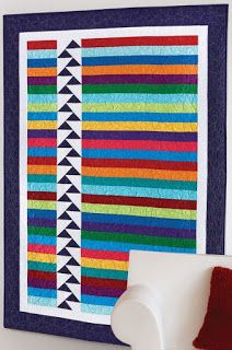 a colorful quilt hanging on the wall next to a white chair