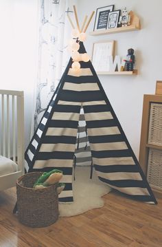 a black and white teepee tent sitting on top of a wooden floor next to a baby crib