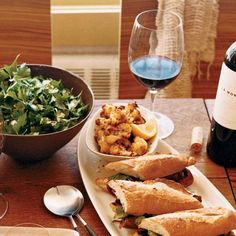 two sandwiches and salad on a white plate with a bottle of wine in the background