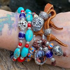 This tribal bracelet is a stunning, whimsical piece featuring genuine Kingman turquoise oval beads and vibrant chevron beads. It boasts an artisan-soldered ceramic haunted house charm, Karen Hill Tribe fine silver beads and link, and an artisan pewter sugar skull button closure. The design includes a pewter sugar skull dangle charm, a bat focal bead, tiny 4mm round red coral beads, carved bone beads, leather cord and soft deer leather. This bracelet has one strand attached to the sugar skull but Handmade Turquoise Bohemian Stretch Bracelet, Bohemian Stretch Bracelet With Round Beads, Handmade Bohemian Turquoise Stretch Bracelet, Nickel-free Turquoise Beaded Bracelets For Festivals, Bohemian Nickel-free Bracelets For Festivals, Bohemian Stretch Bracelet With Colorful Turquoise Beads, Nickel-free Bohemian Festival Bracelet, Bohemian Festival Bracelet Nickel Free, Bohemian Stretch Bracelet With Colorful Beads In Turquoise