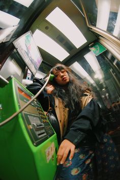 a woman standing next to a green machine on a subway platform with her hair blowing in the wind