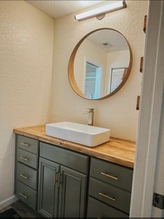 a bathroom sink sitting under a mirror next to a wooden counter top in front of a window