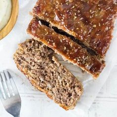 two slices of meatloaf next to a bowl of yogurt and a fork