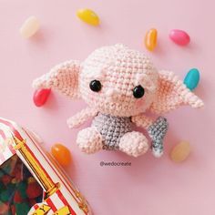 a small crocheted elephant sitting next to a candy bag on a pink surface