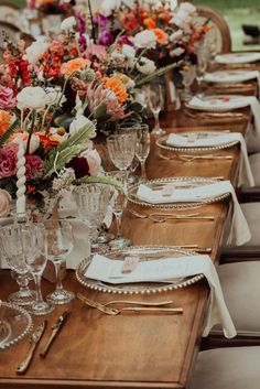 a long wooden table topped with lots of wine glasses and place settings filled with flowers