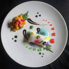 a white plate topped with a piece of cake next to fruit and flowers on top of it