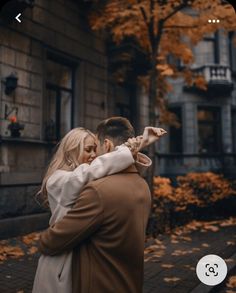 a man and woman standing in front of a building with autumn leaves on the ground