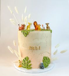 a birthday cake decorated with animals and plants on it's side, sitting on a white surface