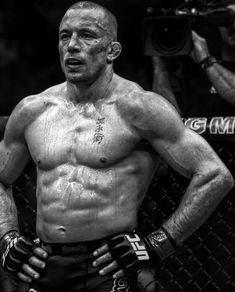 a black and white photo of a man with his hands on his hips standing in front of a chain link fence