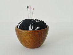 a wooden bowl with two pins in it and some black material on the top, sitting on a white surface