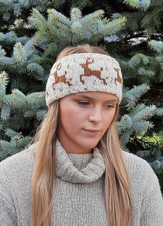 a woman with long hair wearing a knitted headband in front of a pine tree