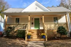 a small white house with green door and steps leading up to the front porch area