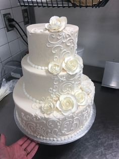 a three tiered white wedding cake with flowers on it, being held by a person