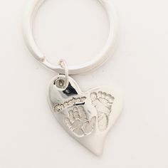 a silver heart shaped keychain with a hand and foot print on the front