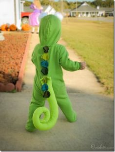 a little boy in a green costume walking down the street with a toy snake on it's back