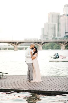 an engaged couple standing on a dock in front of the water and cityscape