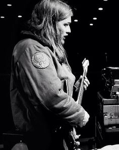 a man with long hair holding a guitar in front of a recording equipment set up