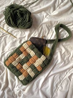 a crocheted purse sitting on top of a bed next to a ball of yarn