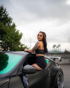 a woman leaning on the hood of a sports car with her hand on the window