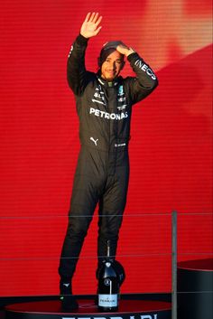 a man standing on top of a podium holding his hands up in the air while wearing a racing suit