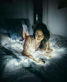 a woman laying on top of a bed under a blanket covered in white light bulbs