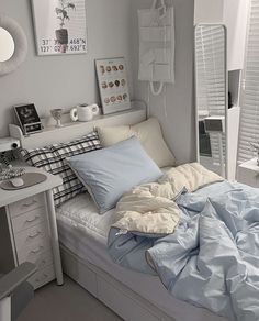 a bed with blue sheets and pillows in a bedroom next to a white dresser, mirror and window