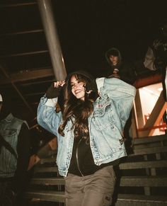 a woman in black shirt and jean jacket walking up stairs with people behind her at night