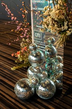 several shiny balls are stacked on top of each other in front of a vase with flowers