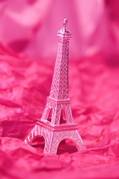 a small pink eiffel tower sitting on top of a red bed sheet in front of a pink background