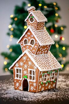 a gingerbread house is sitting in front of a christmas tree with lights on it