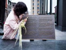 a woman kneeling down next to a plaque with writing on it and flowers in her hand