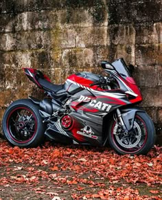 a red and black motorcycle parked in front of a brick wall with leaves on the ground