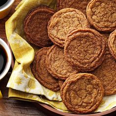 some cookies are on a plate next to two cups of coffee and a yellow napkin