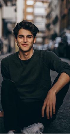 a young man sitting on the ground in front of a building with his legs crossed