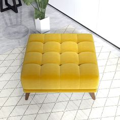 a yellow ottoman sitting on top of a white rug next to a potted plant