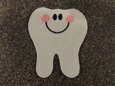 a felt tooth with a smiley face on it's side, sitting on the ground