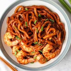 a white bowl filled with shrimp and noodles next to chopsticks on a table